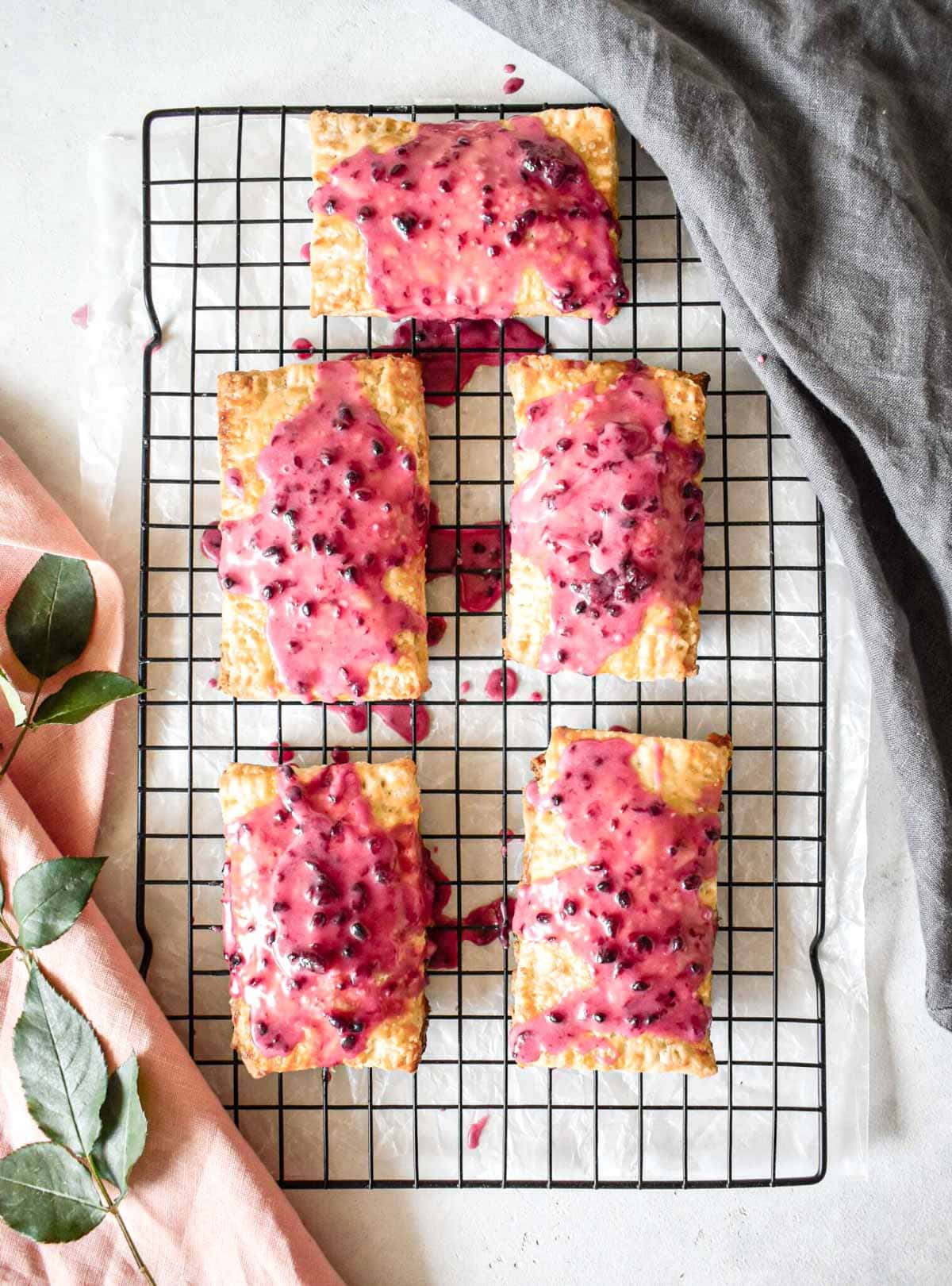 blackberry pop tarts with blackberry glaze on a cooling rack with a pink and grey linens.