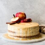 Bourbon Apple Cider Cake topped with apples and cinnimon sticks on a marble platter