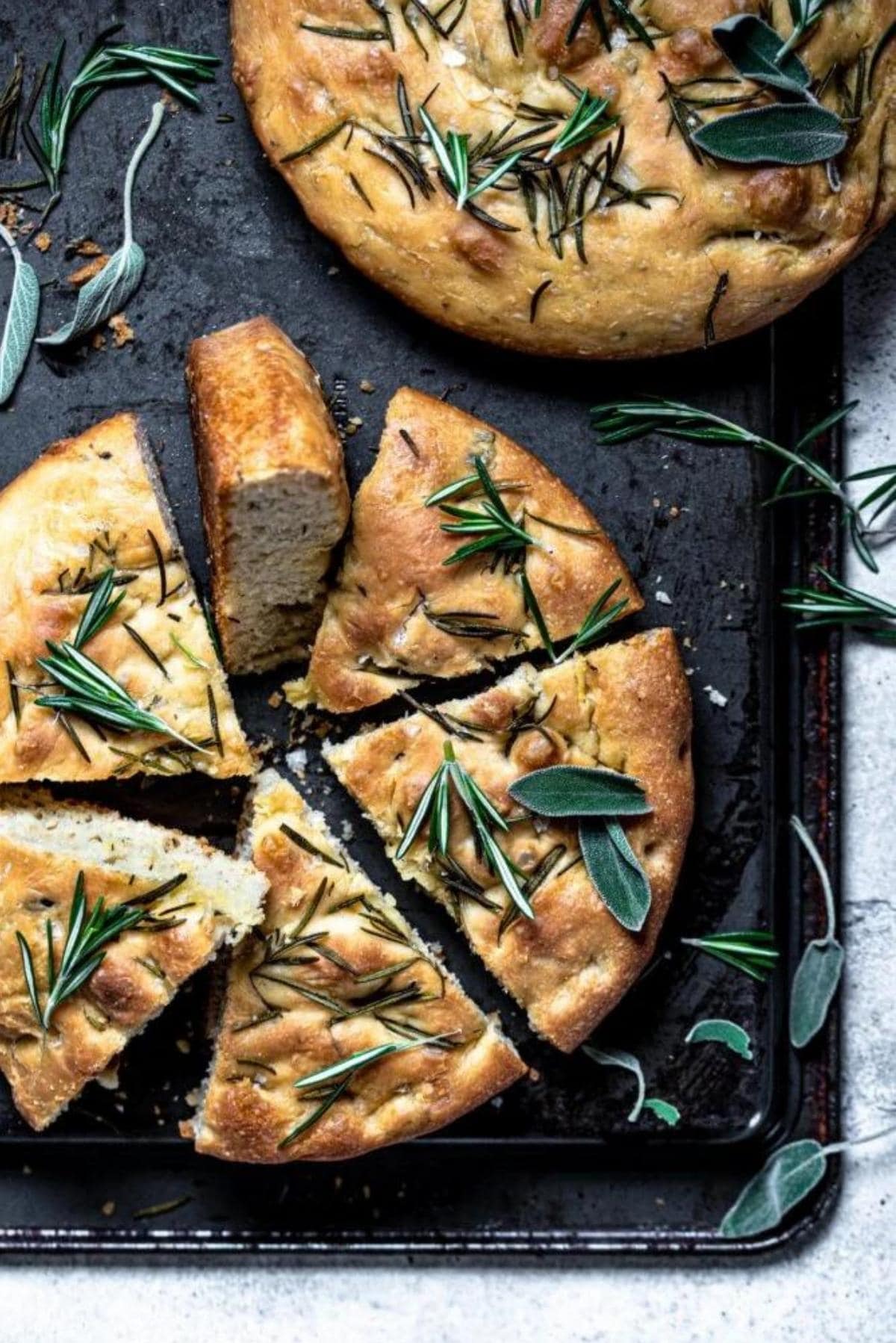 Sliced focaccia bread on a upside down baking sheet and sprinkled with sage.