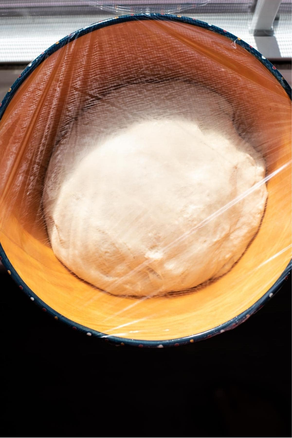 Risen focaccia dough in a orange mixing bowl.