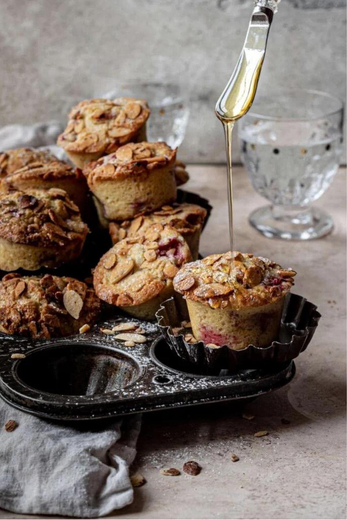 Raspberry almond muffin on a vintage muffin tray, with honey being drizzled on it.