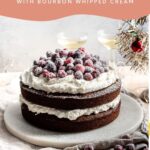 Two layers of gingerbread cake with bourbon whipped cream in-between and on top of each layer. Topped with candied cranberries and on a marble plate.