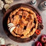 caramel apple pie on a wood cake stand surrounded by apples and pine cones