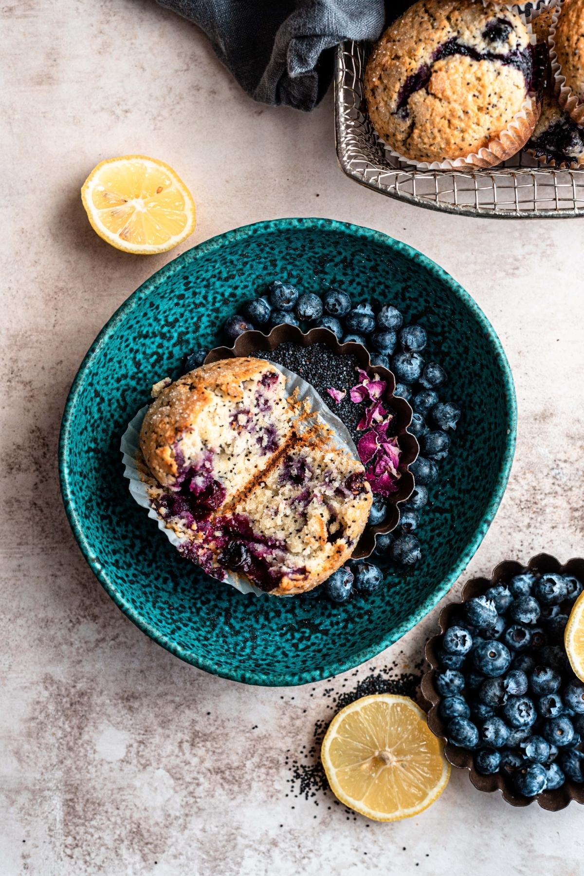 Split muffin in a turquoise bowl with blueberries.