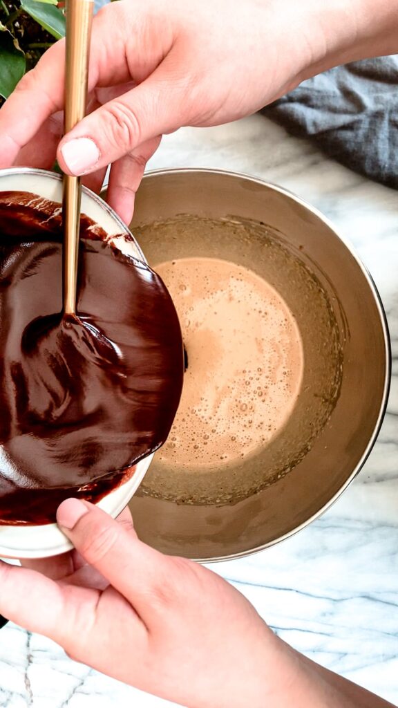 melted chocolate being added to the whipped eggs and sugar