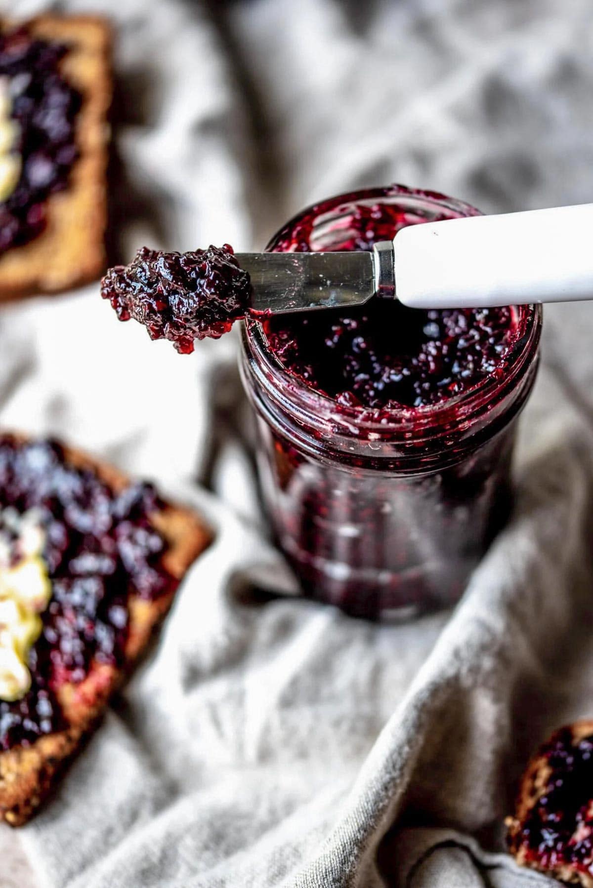 Blackberry jam in small glass jar with a small knife balancing on top of the jar.