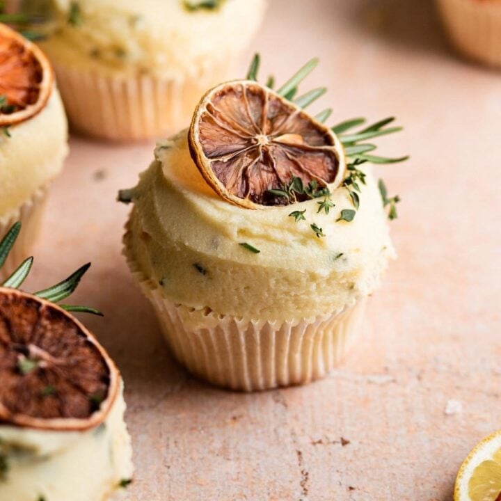 Lemon cupcake decorated with rosemary dried lemon slices on a brown table.
