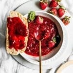 Strawberry jam in a white bowl with a gold spoon.