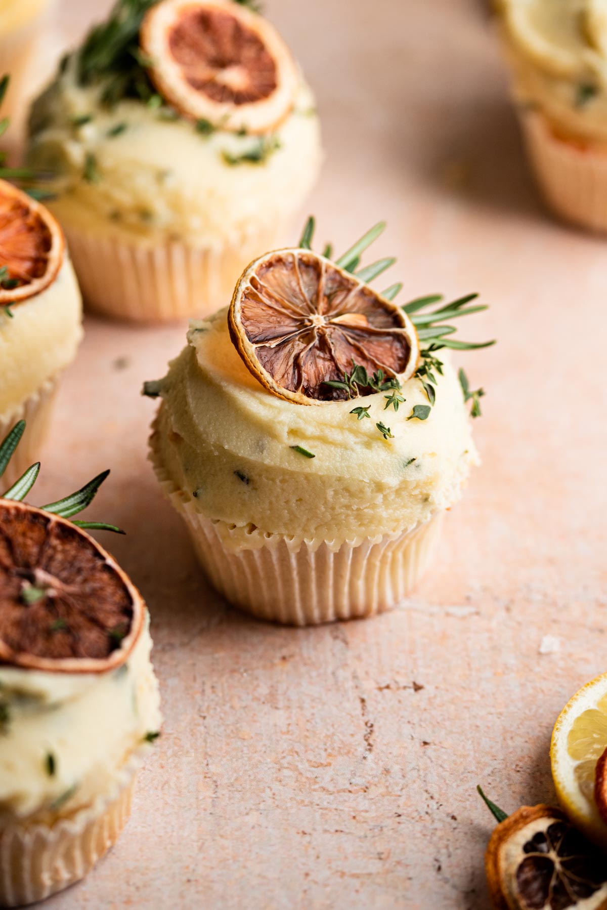 Lemon cupcake decorated with rosemary dried lemon slices on a brown table.