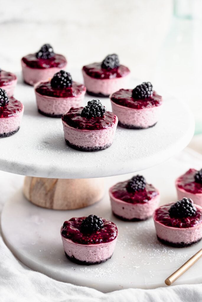 mini blackberry cheesecakes on a cake stand.