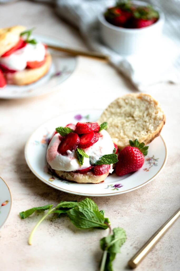 Strawberry shortcake on a floral plate with a mint spring next to it on top of a brown table