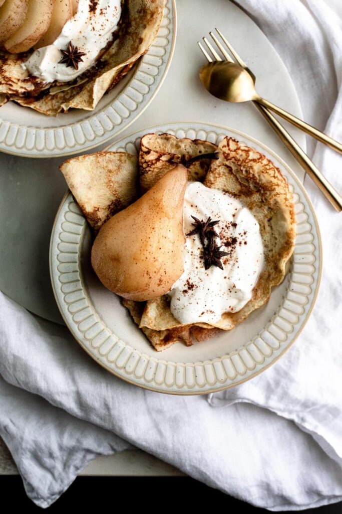 Bourbon Poached pears with folded crepes and whipped cream in a bowl topped with star anise.