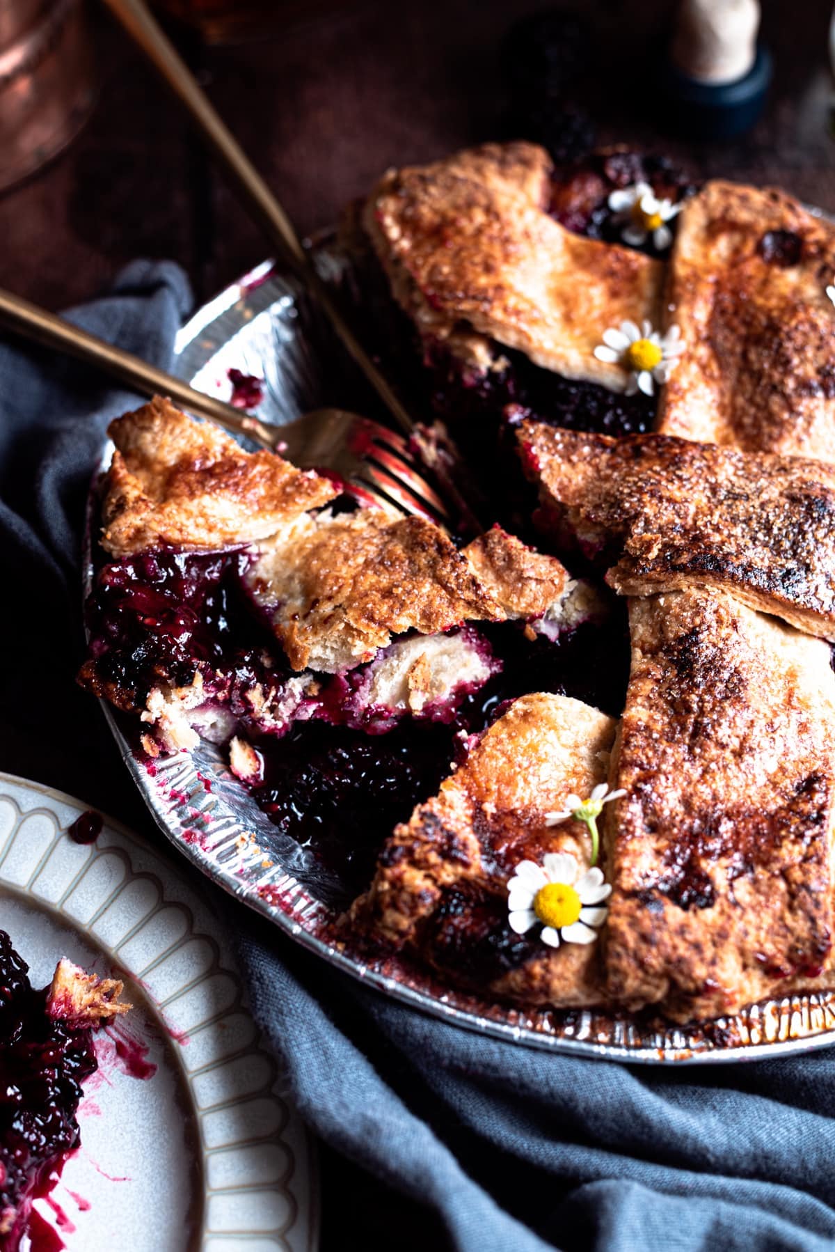 Blackberry pie in a pie tin with a slicing missing and a fork and knife