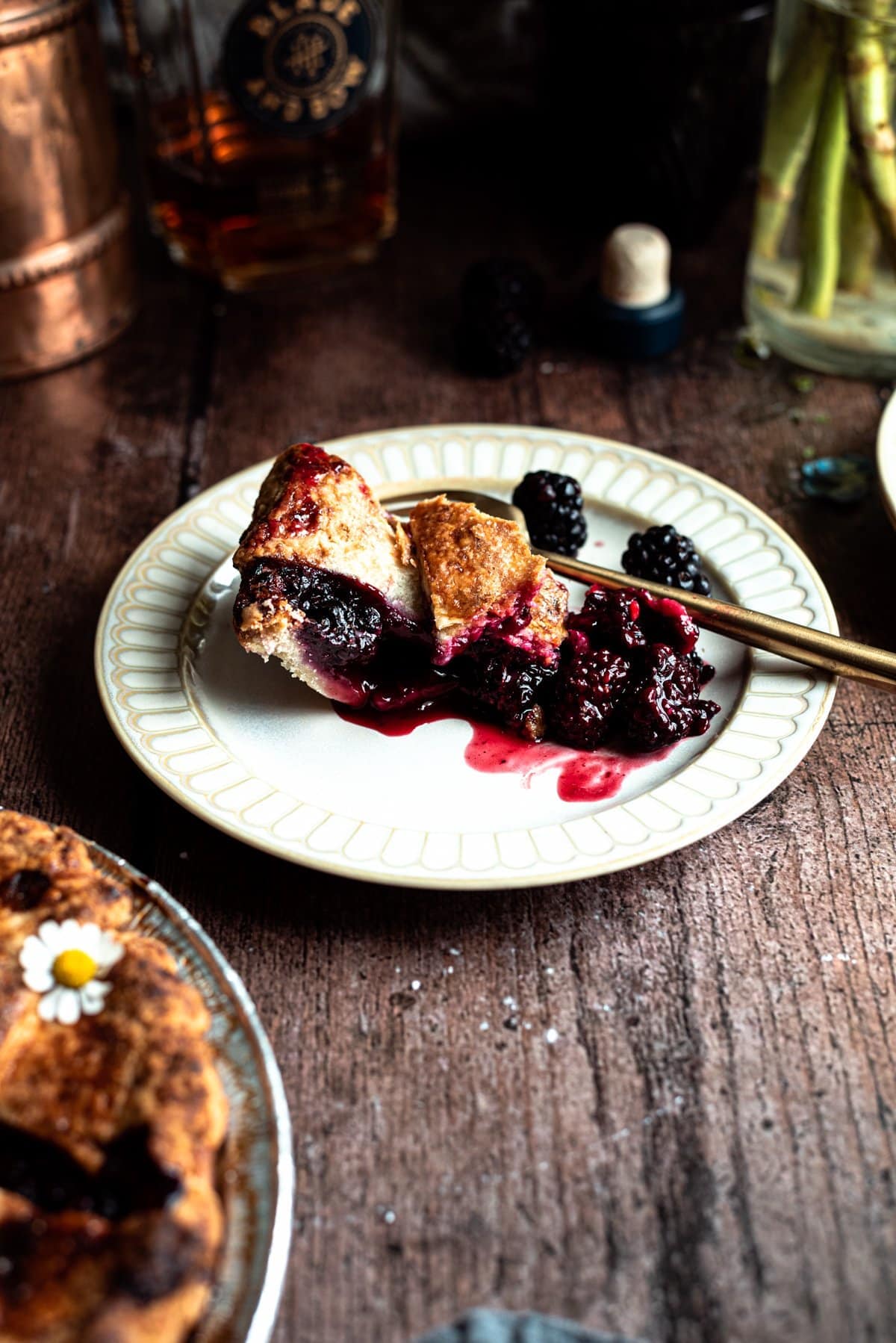 a slice of blackberry pie on a plate with a gold fork on a wood table. 