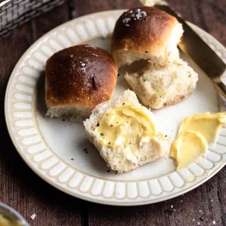 rolls torn in half with butter smeared on them. On a brown plate and on a wooden table.