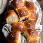 Dinner rolls in a bread basket on a wood table.