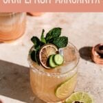 Grapefruit margarita garnished with cucumber and mint on a brown table.