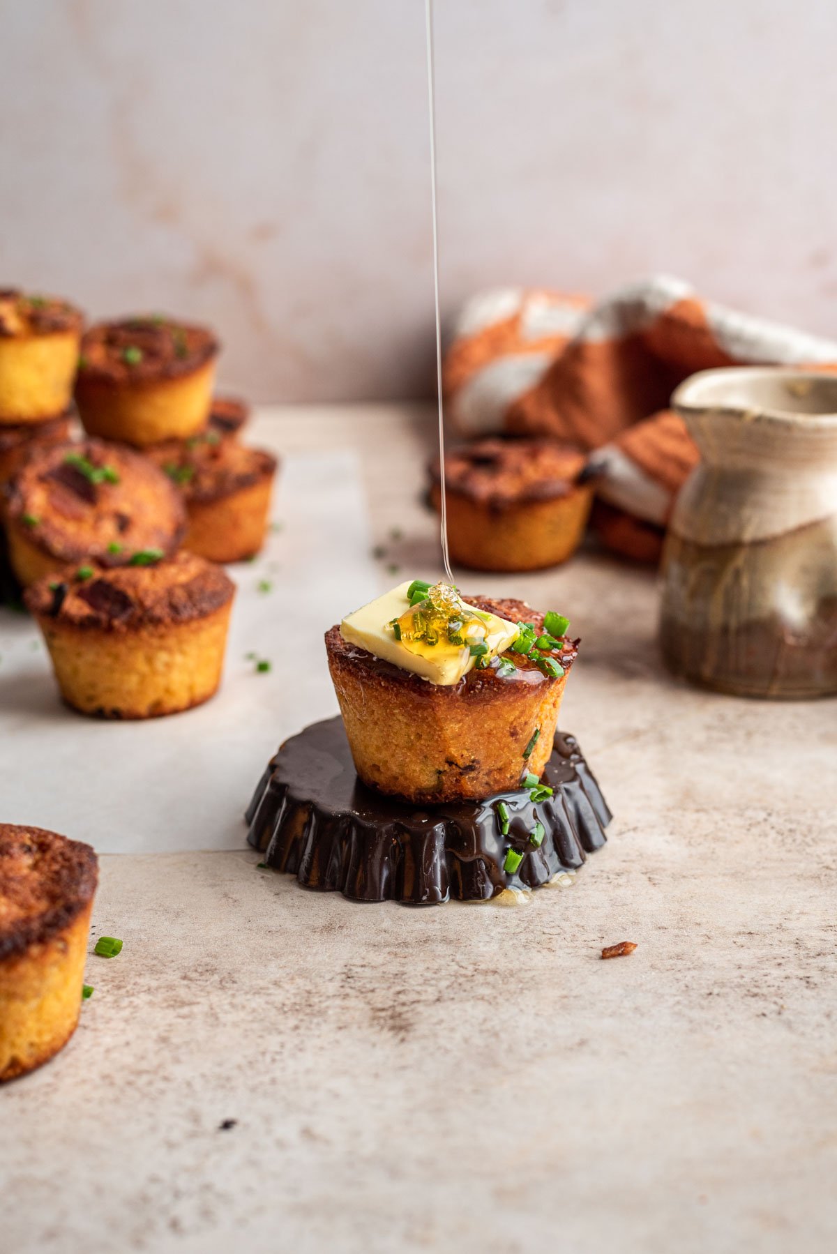 Bacon cornbread muffin topped with butter and chives on a brown table.
