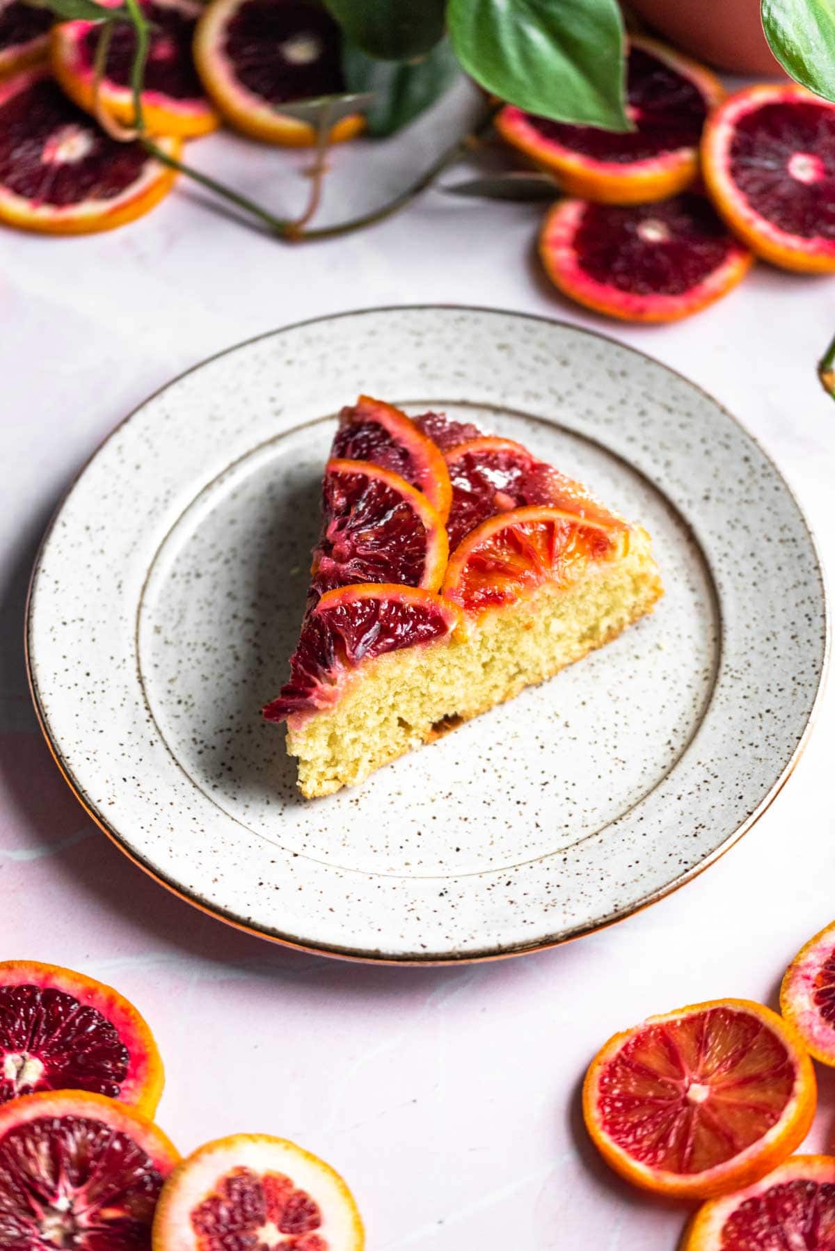 A slice of blood orange upside down cake on a plate and with orange slices in the corner of the photo.