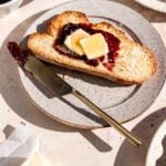 Toasted bread on a speckled plate with jam and two slices of butter on top.