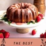 Strawberry pound bunt cake on a marble cake stand with pink strawberry glaze and surrounded by strawberries.