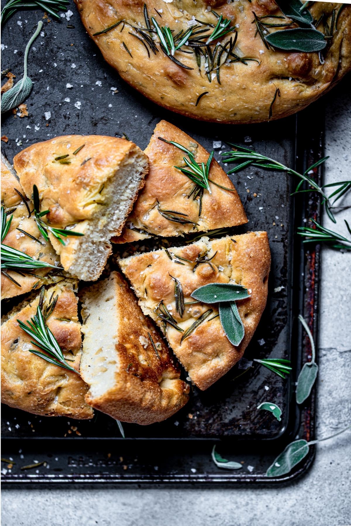 Sliced focaccia bread on a upside down baking sheet and sprinkled with sage.