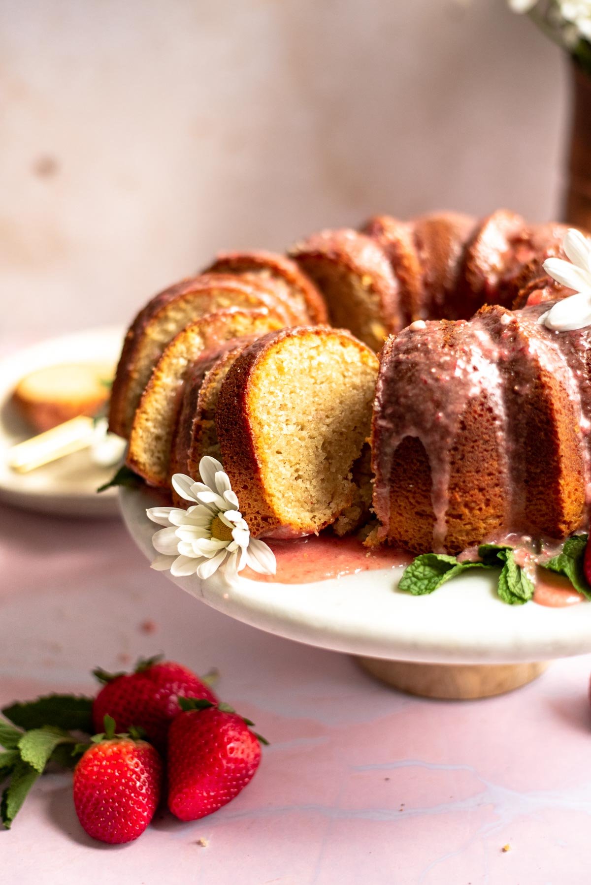 Sliced strawberry pound cake on a marble cake stand with a daisy tucked under a slice.