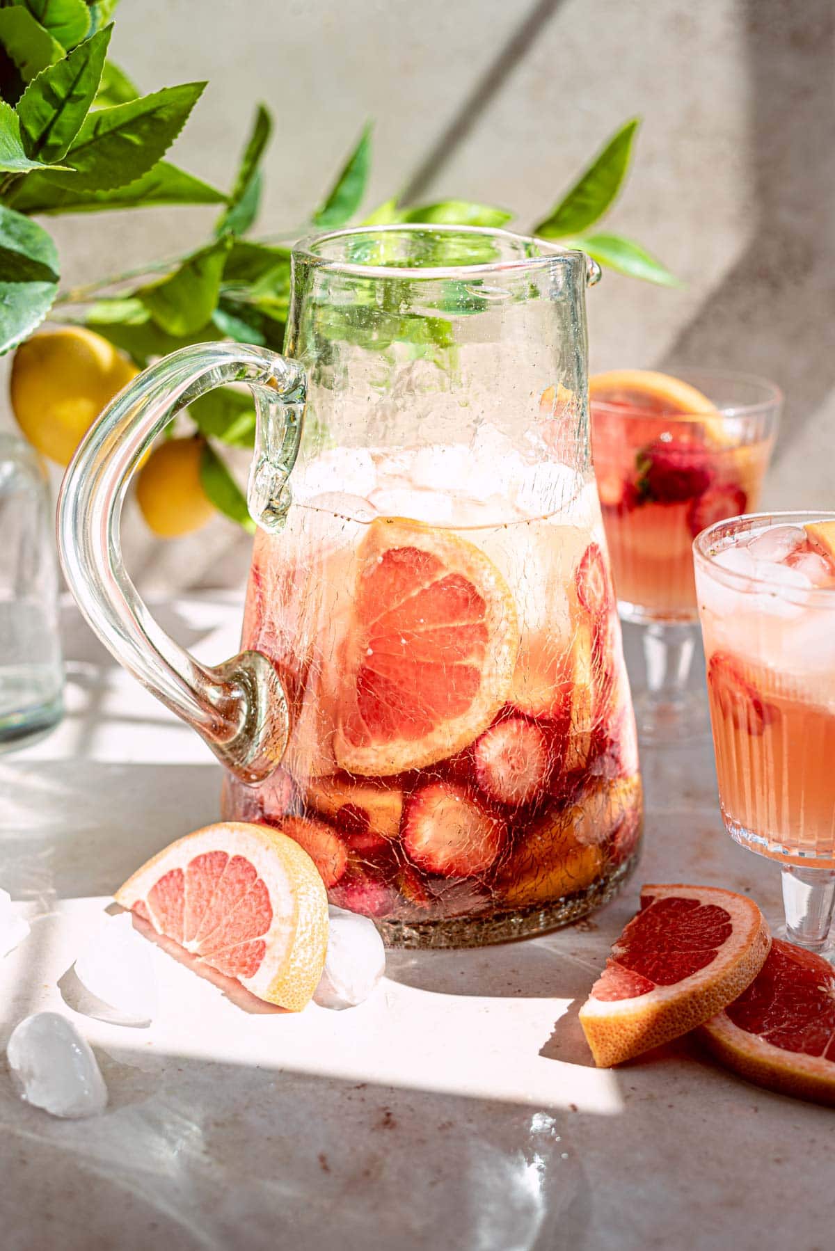 Rose wine sangria in a glass pitcher filled with fruit with glasses off to the sides.