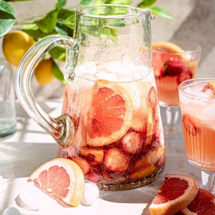 Rose wine sangria in a glass pitcher filled with fruit with glasses off to the sides.