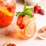 A stemless wine glass on a pink marble table with a pitcher behind it filled with pink sangria.