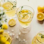 Limoncello spritz in a wine glass with two smaller glasses off to the side. Lemon slices and thyme sprigs are in the glasses.