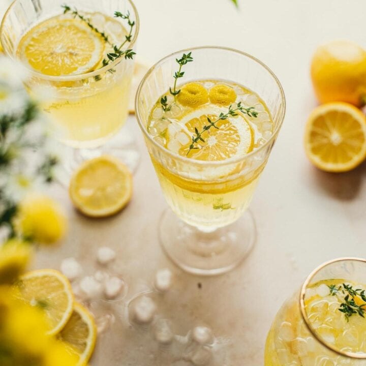 Limoncello spritz in a wine glass with two smaller glasses off to the side. Lemon slices and thyme sprigs are in the glasses.