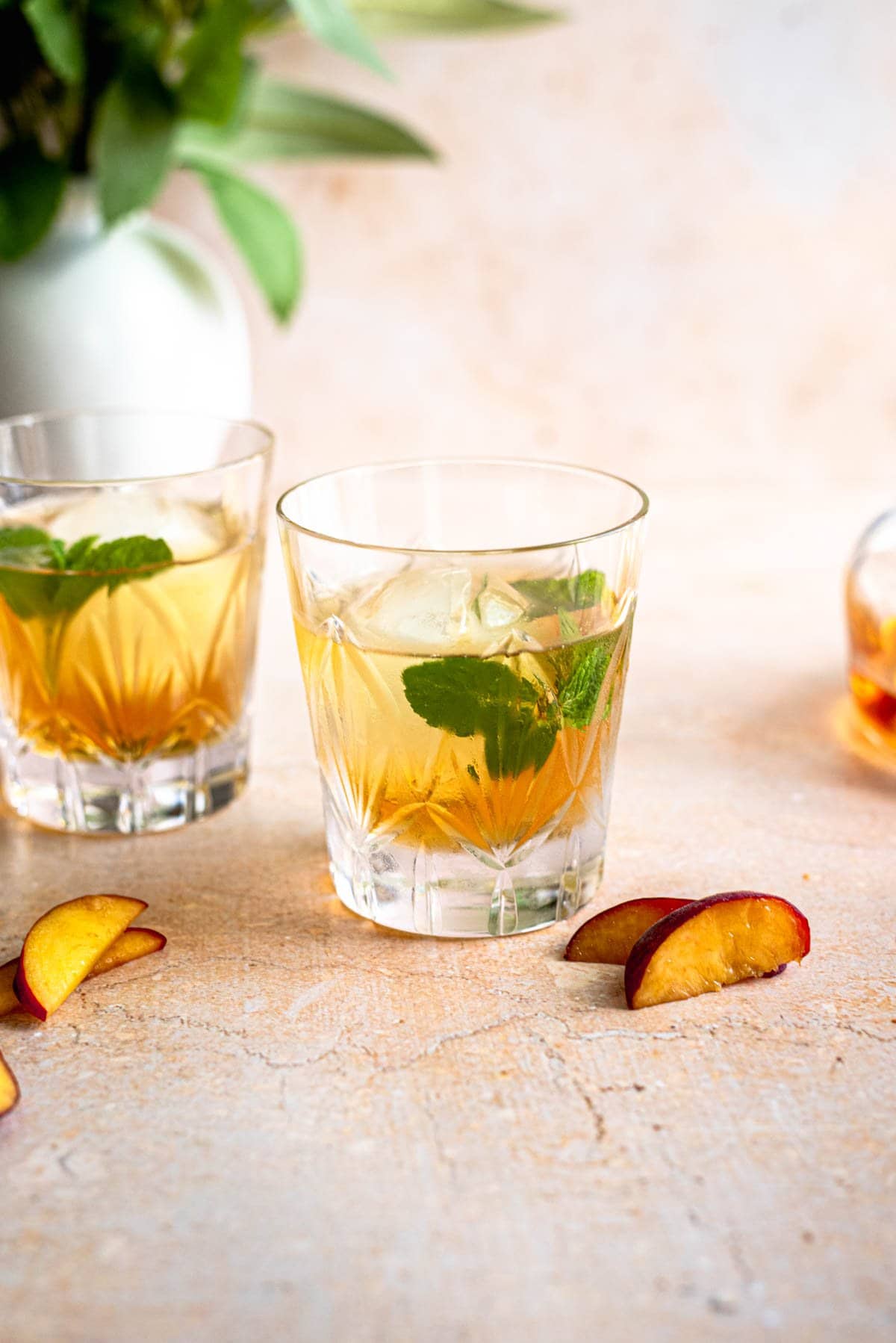 Two glasses of peach old fashioned's on a brown table with peach slices of to the sides.