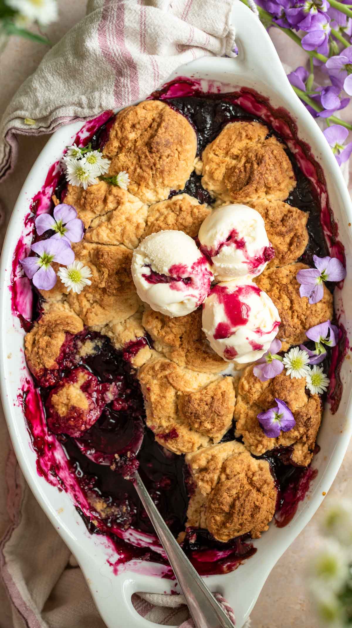 Blueberry cobbler in a baking dish with a scoop taken out and ice cream on top.
