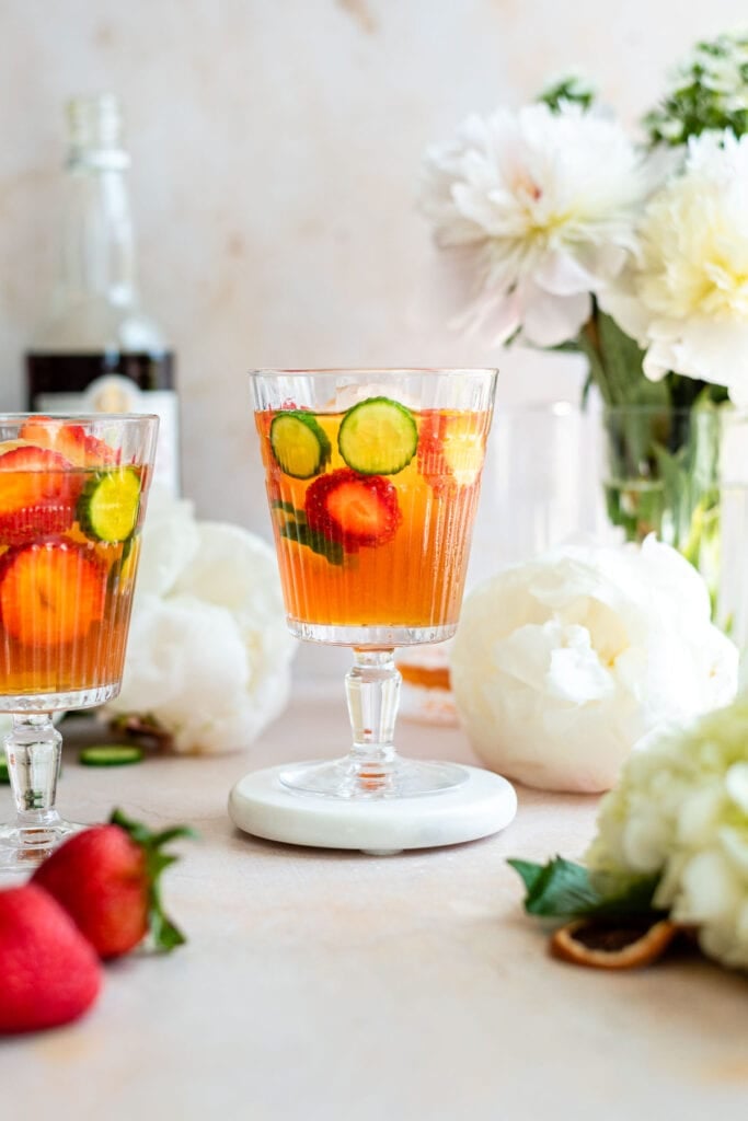 Close up shot of a glass with Pimm's and sliced strawberries and cucumbers.