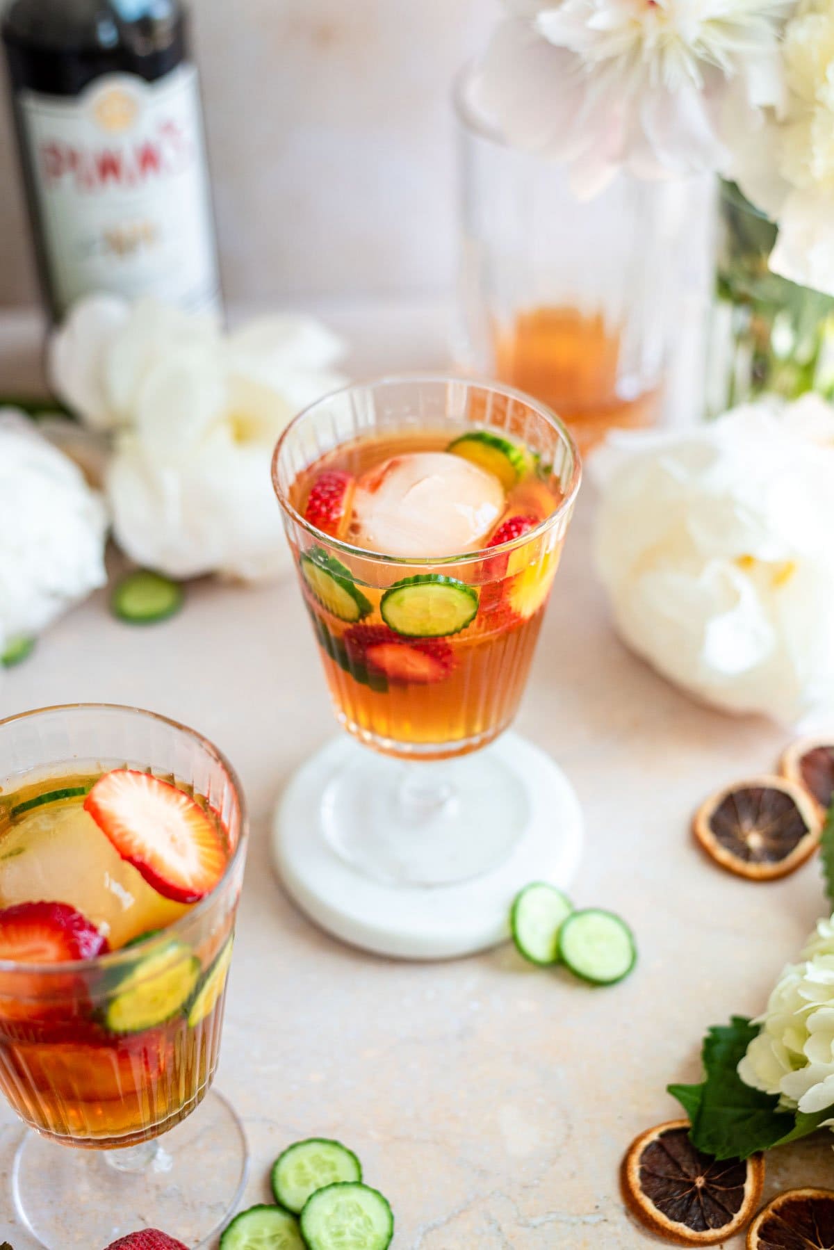Overhead angle shot of two glasses of Pimm's Cups on a brown table surrounded by flowers