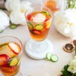 Overhead angle shot of two glasses of Pimm's Cups on a brown table surrounded by flowers.