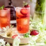 Strawberry bourbon cocktail in a highball glass garnished with strawberry slices and surrounded by white flowers.