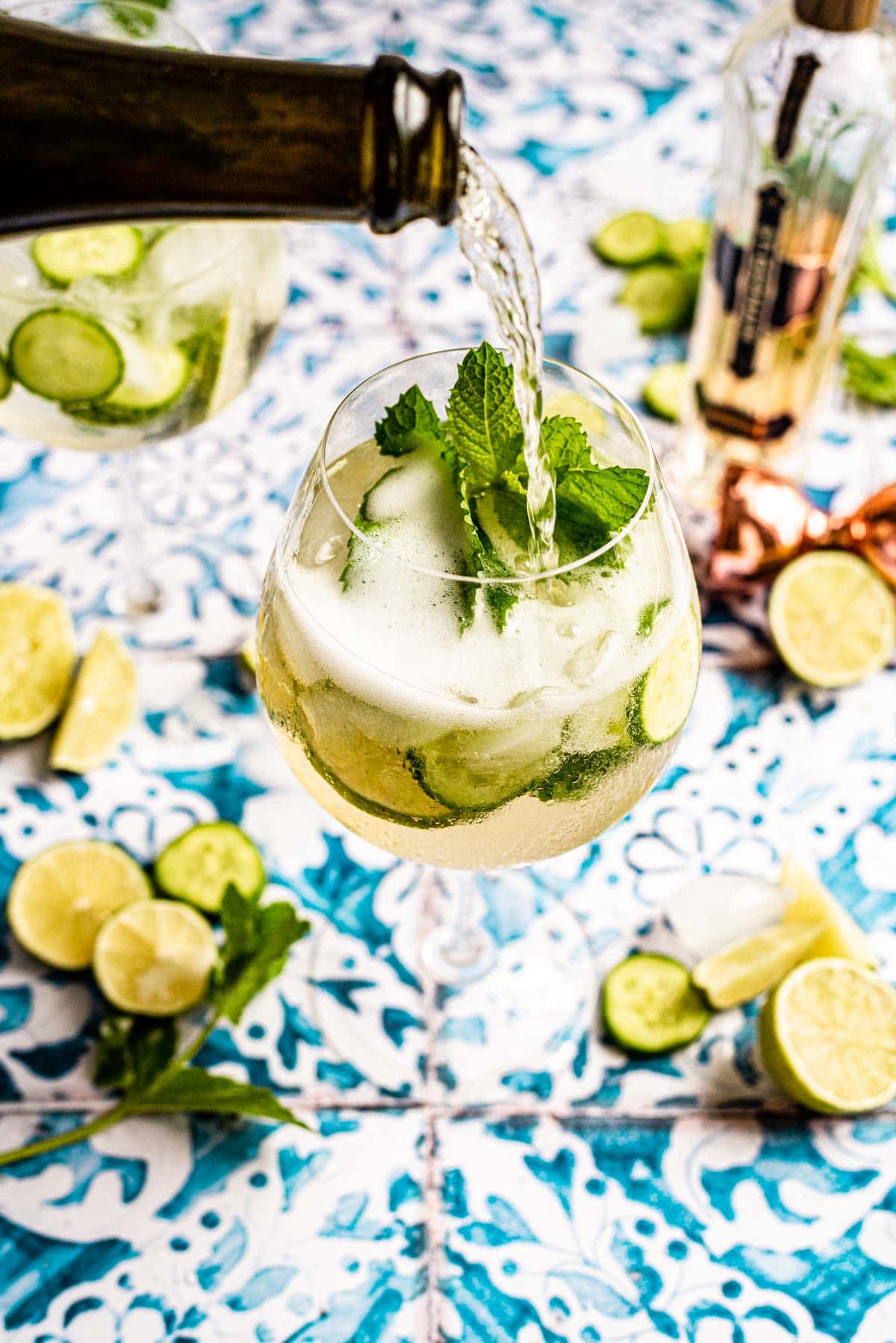 St Germain Spritz on a blue printed tile table garnished with mint, cucumber, and lime.