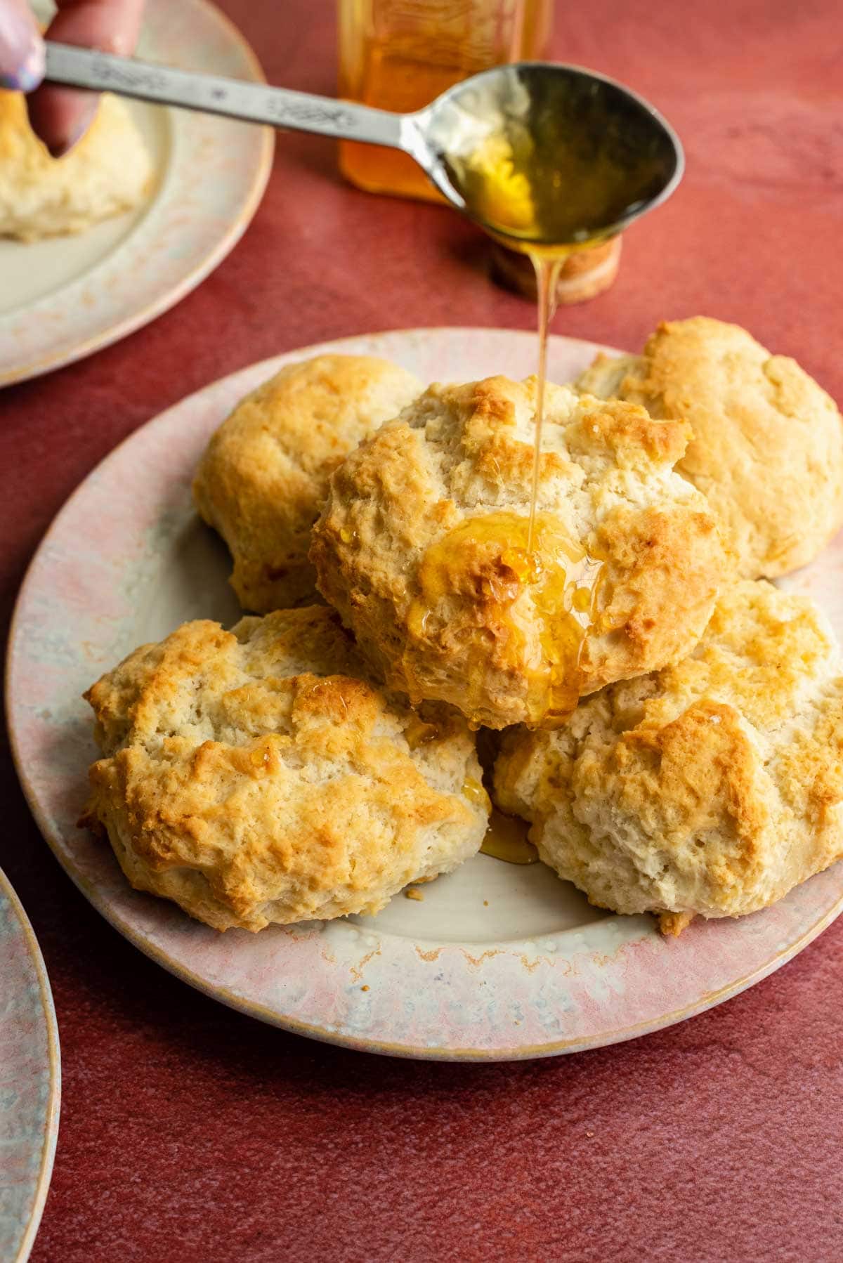 Three ingredient biscuits on a pink plate and being drizzled with honey on a red table.