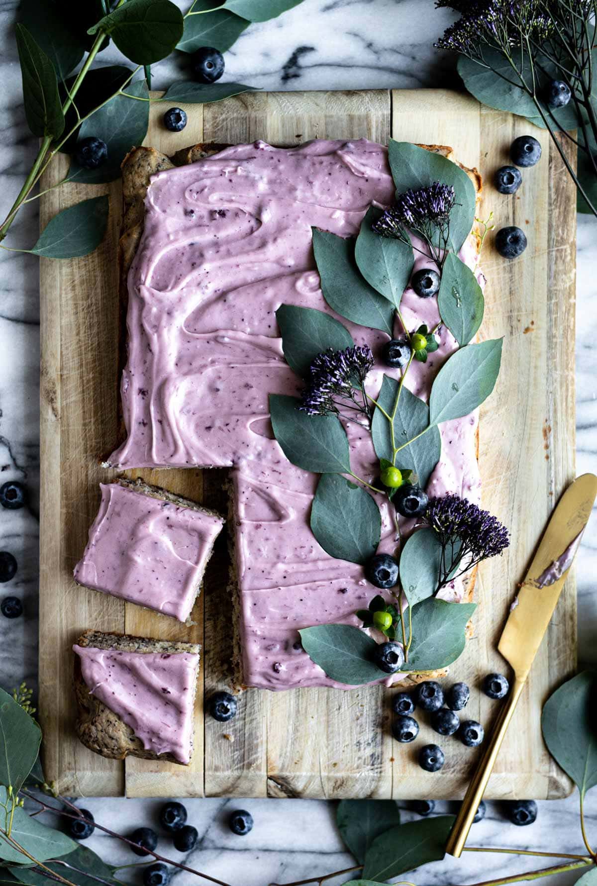 Blueberry sheet cake on a wood cutting board and decorated with blueberries and vines.