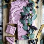 Blueberry sheet cake on a wood cutting board and decorated with blueberries and vines.