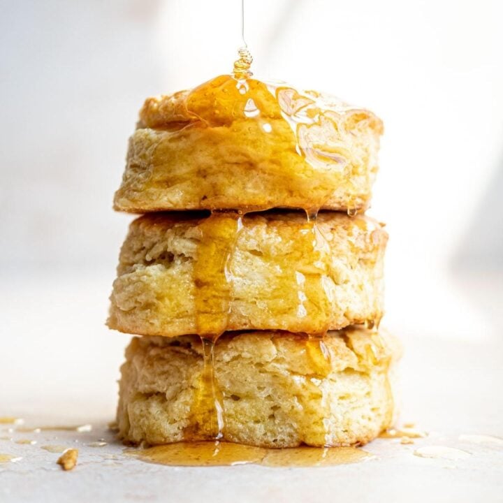Three stacked biscuits with honey drizzling down from the top.