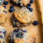Blueberry biscuits on a brown parchment paper surrounded by blueberries.