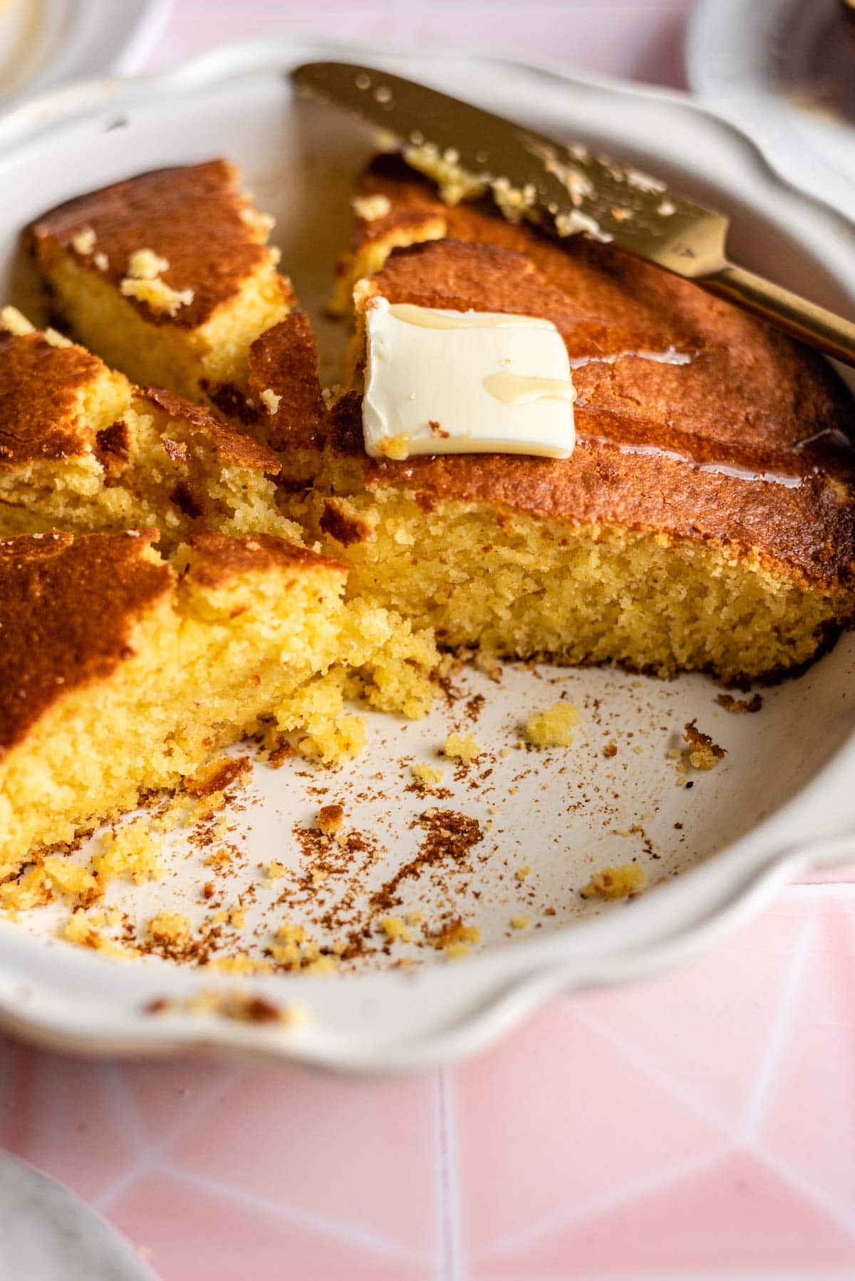 Cornbread in a white baking dish cut into slices with butter on top.