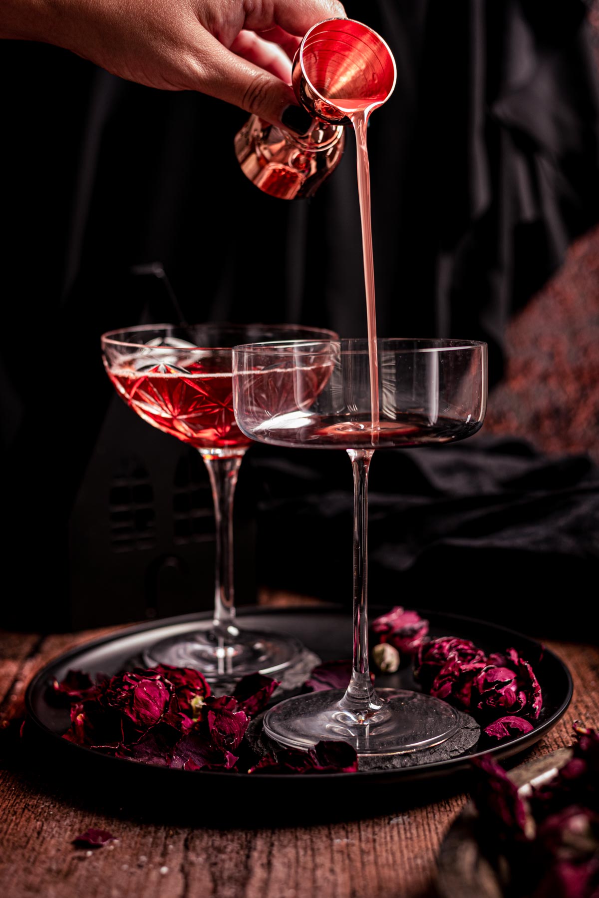 Two coupe glass with rose syrup bring poured into one.