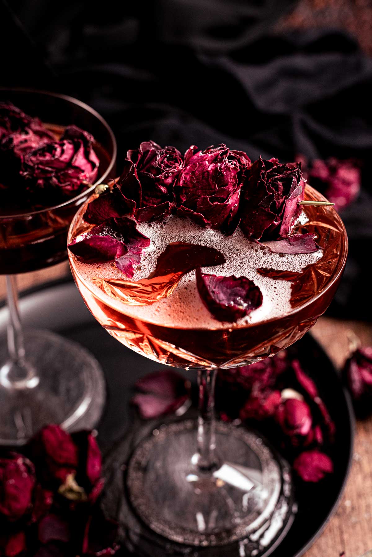 Gomez and Morticia cocktail in coupe glass garnished with dried roses.