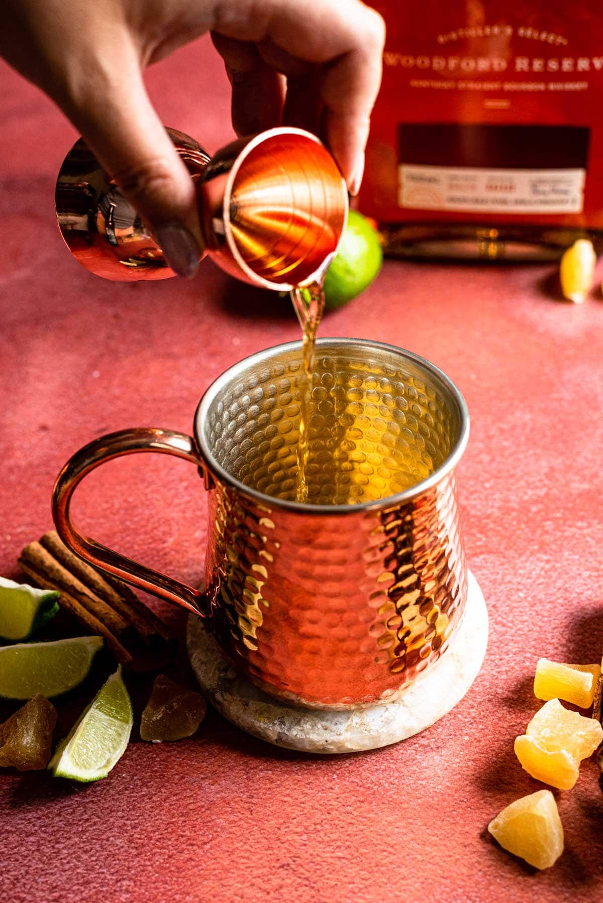 The bourbon being poured into a copper mug on a red stone table.