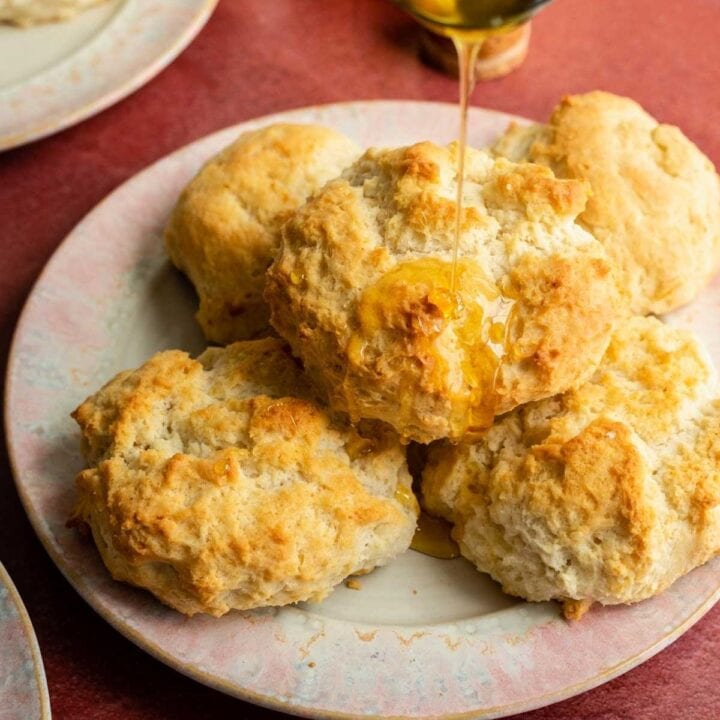 Three ingredient biscuits on a pink plate and being drizzled with honey on a red table.
