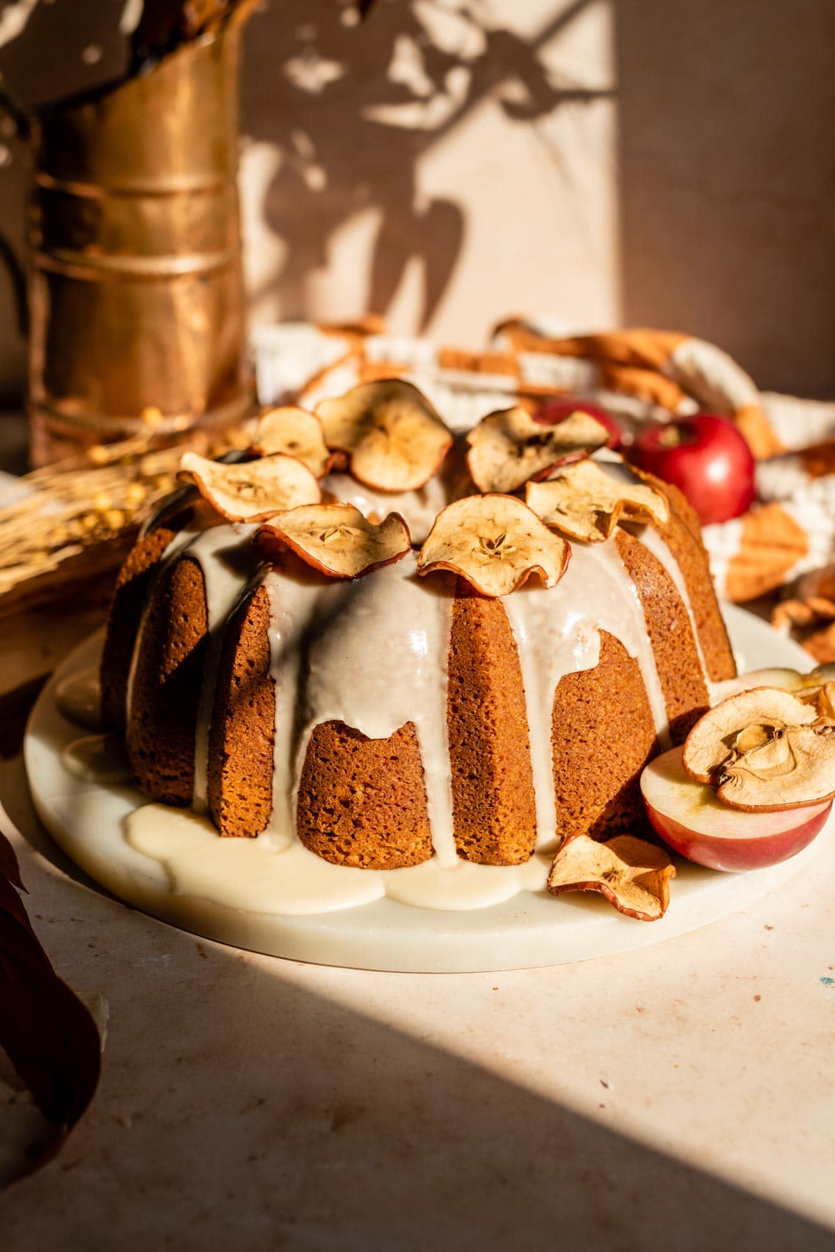 Apple Butter Pound cake on a marble slab with an apple glaze. Its then topped with dried apple slices and is on a brown stone background.